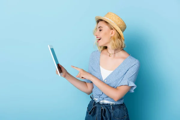 Mujer excitada en sombrero de paja apuntando con el dedo a la tableta digital en azul - foto de stock