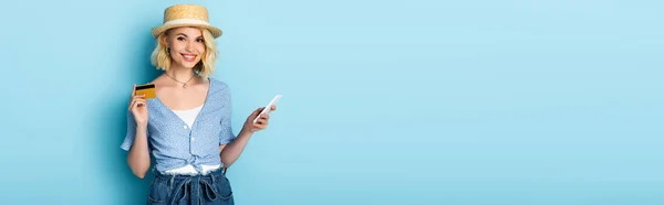 Panoramic crop of woman in straw hat holding credit card and smartphone on blue — Stock Photo