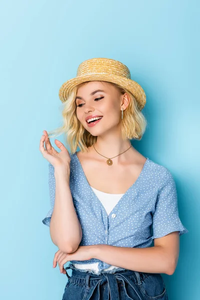 Mujer joven en sombrero de paja haciendo gestos y mirando hacia otro lado en azul - foto de stock