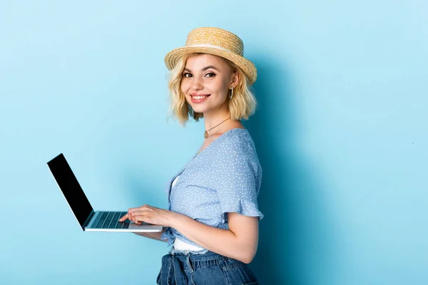 Mujer joven en sombrero de paja usando el ordenador portátil en azul - foto de stock