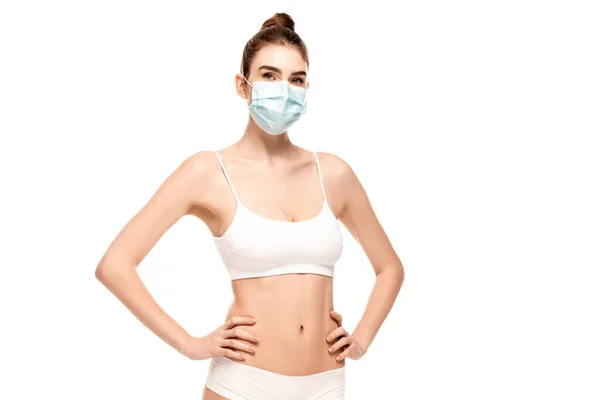 Jeune femme en masque médical, haut et culotte debout avec les mains sur les hanches isolées sur blanc — Photo de stock