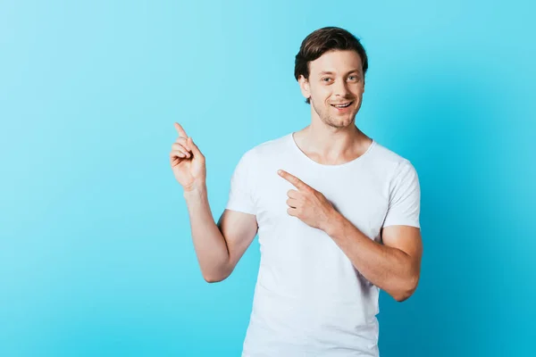 Homme en t-shirt blanc pointant avec les doigts sur fond bleu — Photo de stock