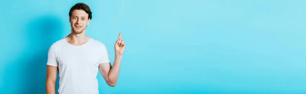 Panoramaaufnahme eines Mannes im weißen T-Shirt, der mit dem Finger auf blauem Hintergrund zeigt — Stockfoto