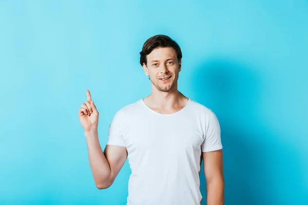 Uomo in t-shirt bianca punta con dito su sfondo blu — Foto stock