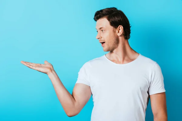 Homme en t-shirt blanc pointant à la main sur fond bleu — Photo de stock