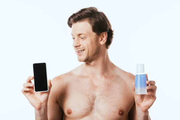 Hombre sin camisa sosteniendo teléfono inteligente con pantalla en blanco y botella de loción aislada en blanco - foto de stock