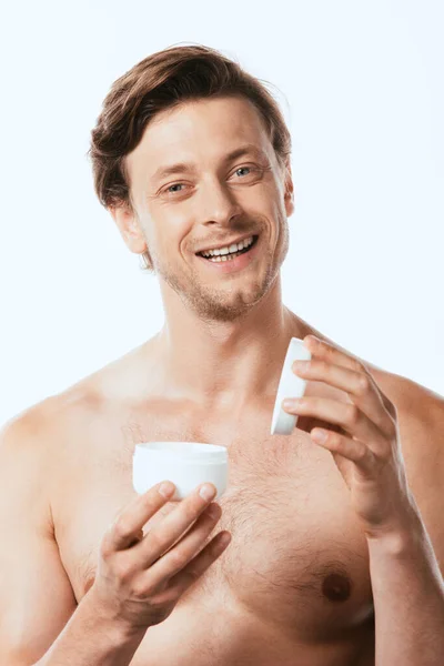 Hombre sin camisa sosteniendo tarro de crema cosmética y mirando a la cámara aislada en blanco - foto de stock