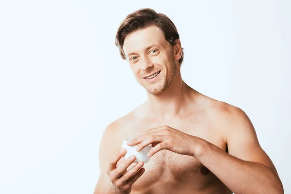 Hombre joven sin camisa mirando a la cámara mientras sostiene el frasco de crema cosmética aislado en blanco - foto de stock