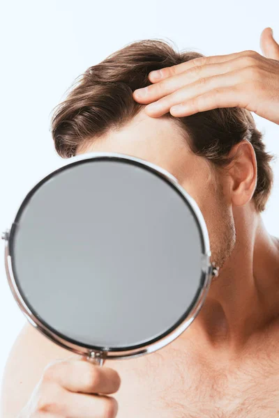 Focus selettivo dell'uomo senza maglietta che tocca i capelli mentre tiene lo specchio isolato sul bianco — Foto stock