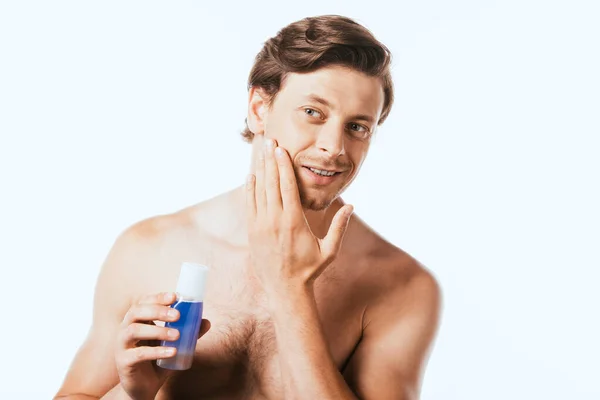 Uomo senza maglietta toccare la pelle, mentre tenendo bottiglia di toner isolato su bianco — Foto stock