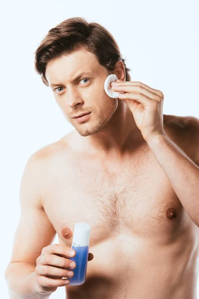 Uomo senza camicia che applica toner con batuffolo di cotone sul viso isolato su bianco — Foto stock