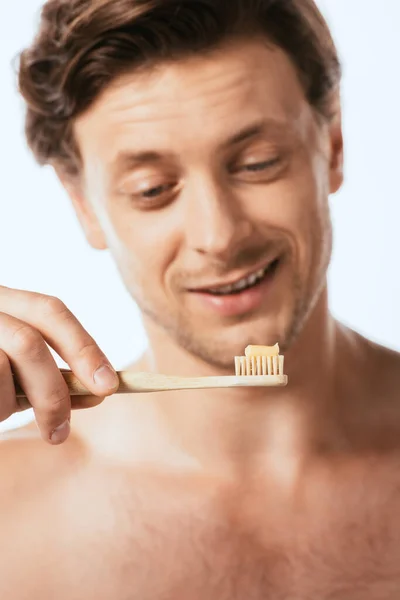 Selective focus of shirtless man looking at toothbrush with toothpaste isolated on white — Stock Photo