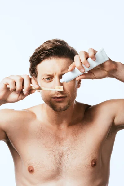 Hombre sin camisa sosteniendo pasta de dientes y cepillo de dientes aislados en blanco - foto de stock