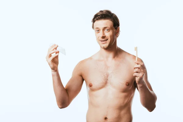 Homme torse nu regardant la caméra tout en tenant brosse à dents et dentifrice isolé sur blanc — Photo de stock