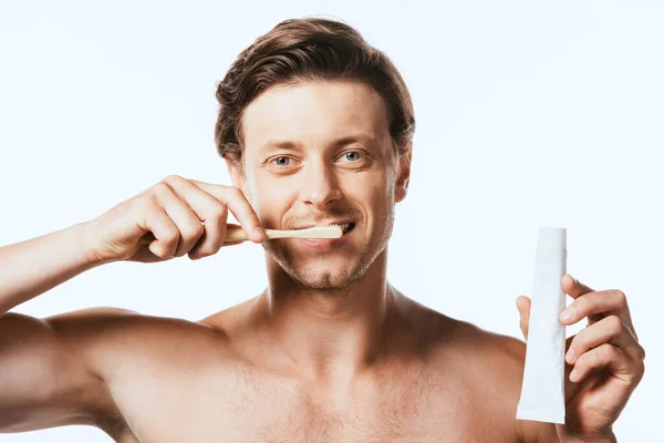 Hombre musculoso mostrando pasta de dientes mientras se cepilla los dientes aislados en blanco - foto de stock