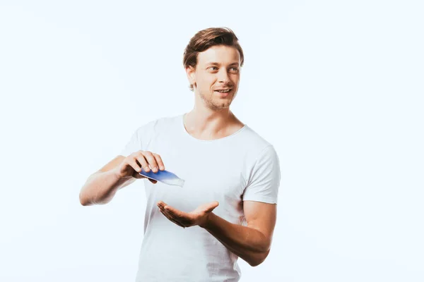 Jeune homme regardant loin tout en versant de la lotion à la main isolé sur blanc — Photo de stock