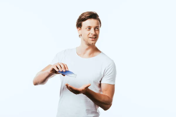 Joven mirando hacia otro lado mientras se vierte loción en la mano aislado en blanco - foto de stock