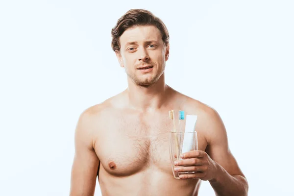 Muscular man holding glass with toothbrushes and toothpaste isolated on white — Stock Photo