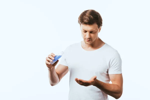 Young man holding bottle of lotion and looking at hand isolated on white — Stock Photo