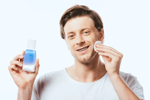 Young man applying lotion with cotton pad isolated on white — Stock Photo