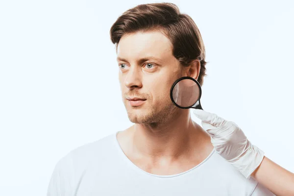 Young man looking away near dermatologist with magnifying glass isolated on white — Stock Photo