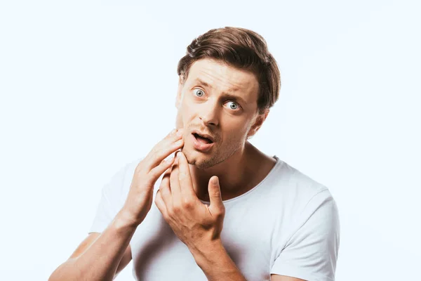 Shocked man touching skin on cheek and looking at camera isolated on white — Stock Photo
