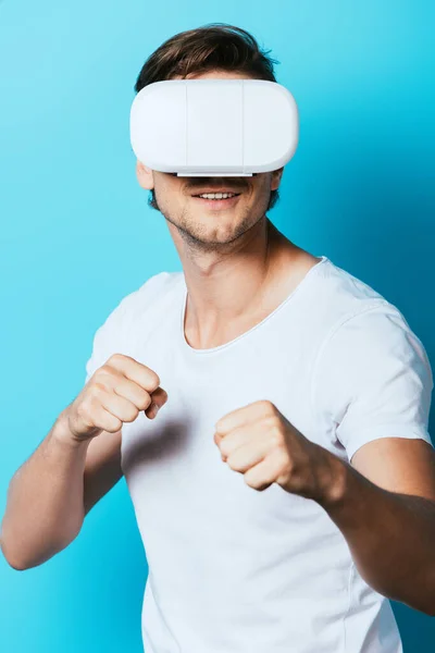 Young man in virtual reality headset showing fists on blue background — Stock Photo