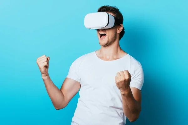 Hombre en auriculares vr mostrando sí gesto sobre fondo azul - foto de stock