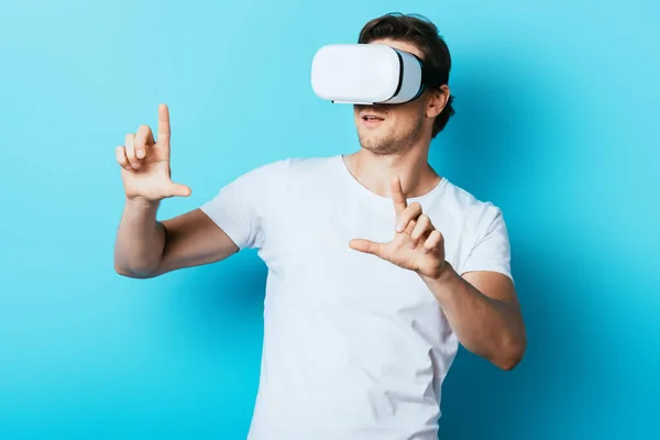 Joven apuntando con los dedos mientras usa auriculares de realidad virtual sobre fondo azul - foto de stock