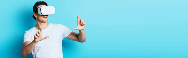 Horizontal crop of man in vr headset pointing with fingers on blue background — Stock Photo