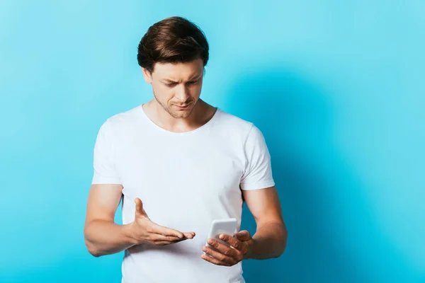 Young man pointing with hand while using smartphone on blue background — Stock Photo