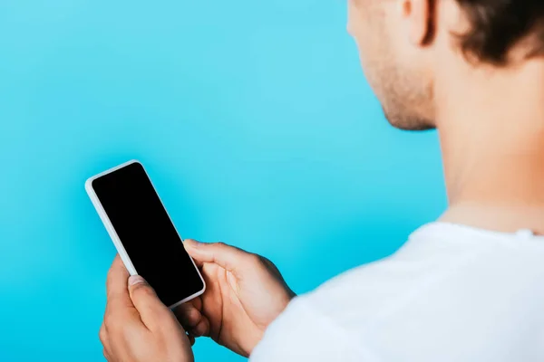 Vista recortada del joven sosteniendo teléfono inteligente con pantalla en blanco aislado en azul - foto de stock