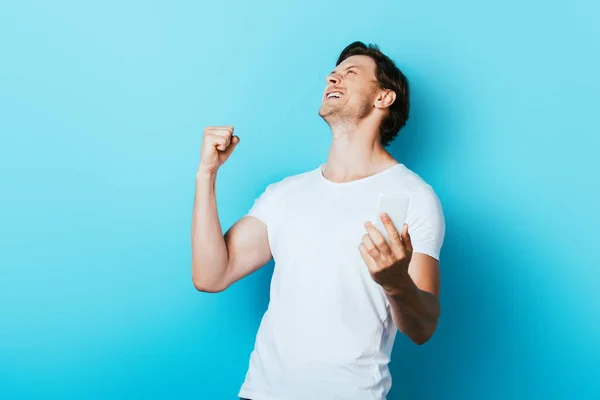 Young man showing yes gesture while holding smartphone on blue background — Stock Photo