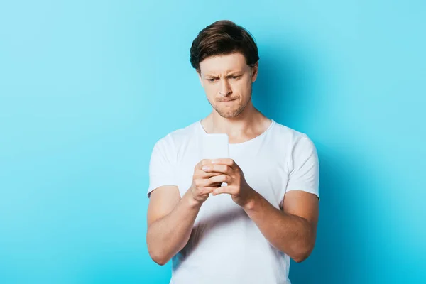 Pensive man using smartphone on blue background — Stock Photo