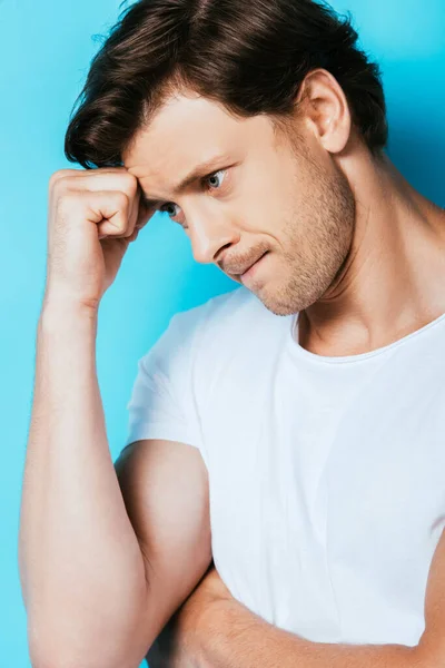 Hombre pensativo en camiseta blanca mirando hacia otro lado sobre fondo azul - foto de stock