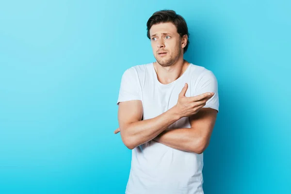 Confused man pointing with hand while looking away on blue background — Stock Photo