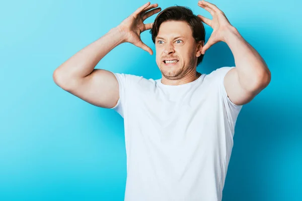 Homme en colère en t-shirt blanc regardant loin sur fond bleu — Photo de stock