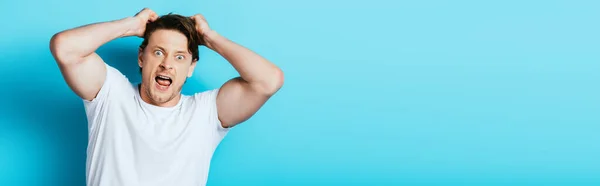 Panoramic orientation of crazy man in white t-shirt looking at camera on blue background — Stock Photo