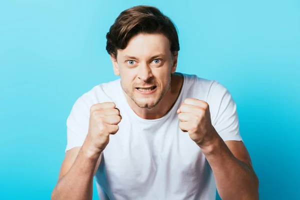 Агрессивный мужчина в белой футболке показывает кулаки на синем фоне — стоковое фото