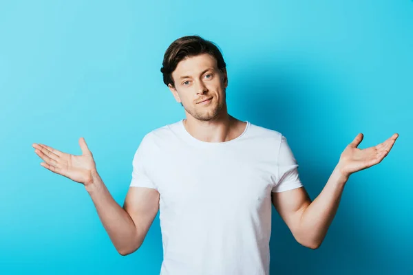 Мужчина в белой футболке пожимает плечами на синем фоне — стоковое фото