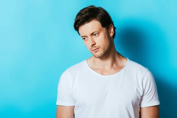 Upset man in white t-shirt looking away on blue background — Stock Photo