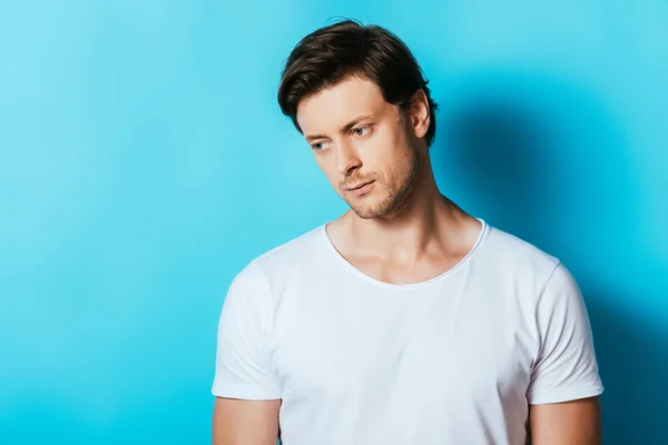 Hombre trastornado en camiseta blanca mirando hacia otro lado sobre fondo azul - foto de stock