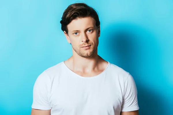 Hombre confiado en camiseta blanca mirando a la cámara sobre fondo azul - foto de stock