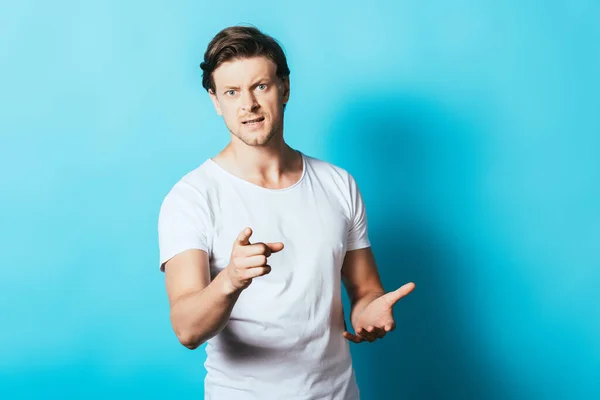 Angry man pointing with finger at camera on blue background — Stock Photo