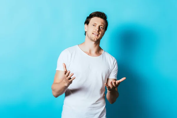 Homme confiant en t-shirt blanc pointant les mains vers la caméra sur fond bleu — Photo de stock