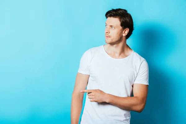 Selbstbewusster Mann im weißen T-Shirt zeigt mit dem Finger auf blauem Hintergrund — Stockfoto