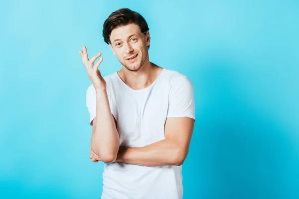 Junger Mann im weißen T-Shirt gestikuliert und blickt in die Kamera auf blauem Hintergrund — Stockfoto