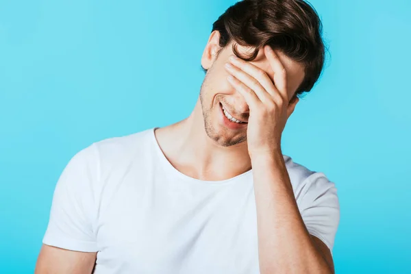 Giovane uomo in t-shirt bianca che copre gli occhi con mano isolata su blu — Foto stock