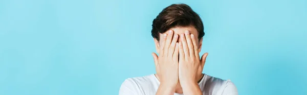 Panoramic shot of man covering face with hands on blue background — Stock Photo