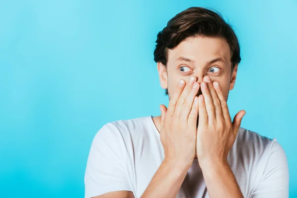 Hombre sorprendido cubriendo la boca con las manos aisladas en azul - foto de stock